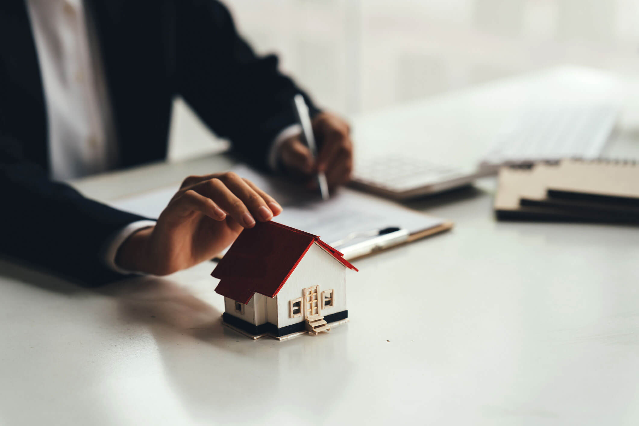 Una persona tocando una casa en miniatura apoyada sobre una mesa