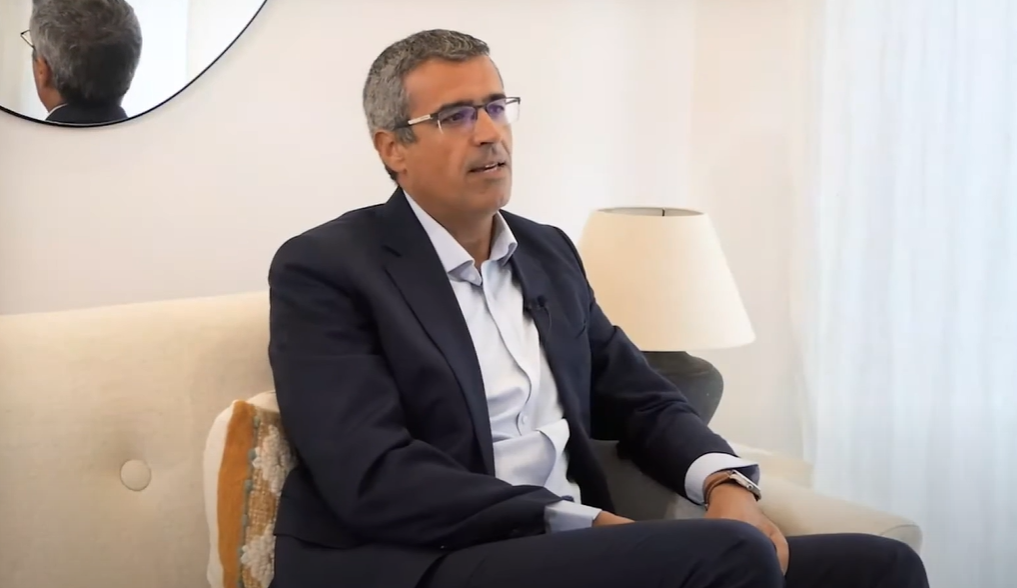 Hombre con traje participando en una entrevista en entorno corporativo, sentado en una silla junto a una planta decorativa